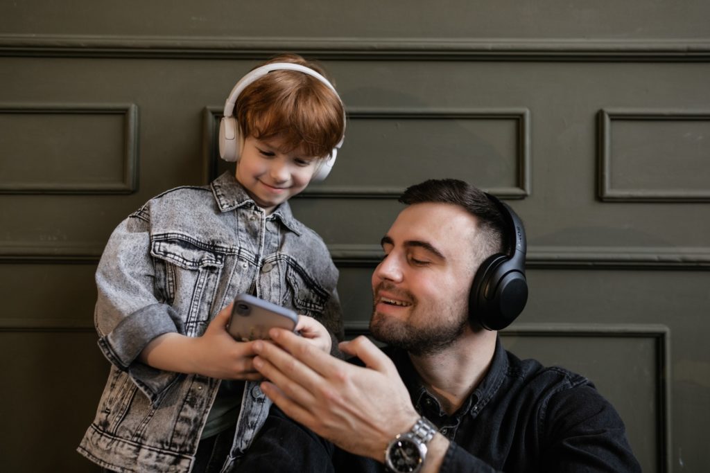 man and son look at smartphone while having headphones on