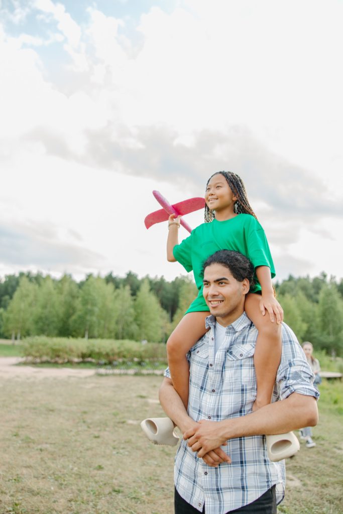 daughter sitting on father's shoulders while holding an airplane