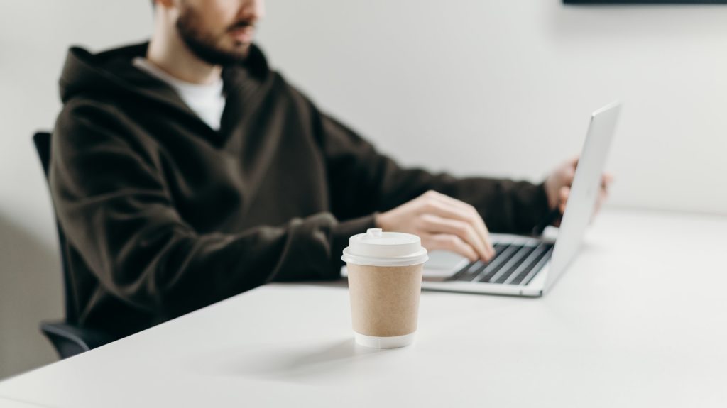 coffee cup in focus while man uses laptop