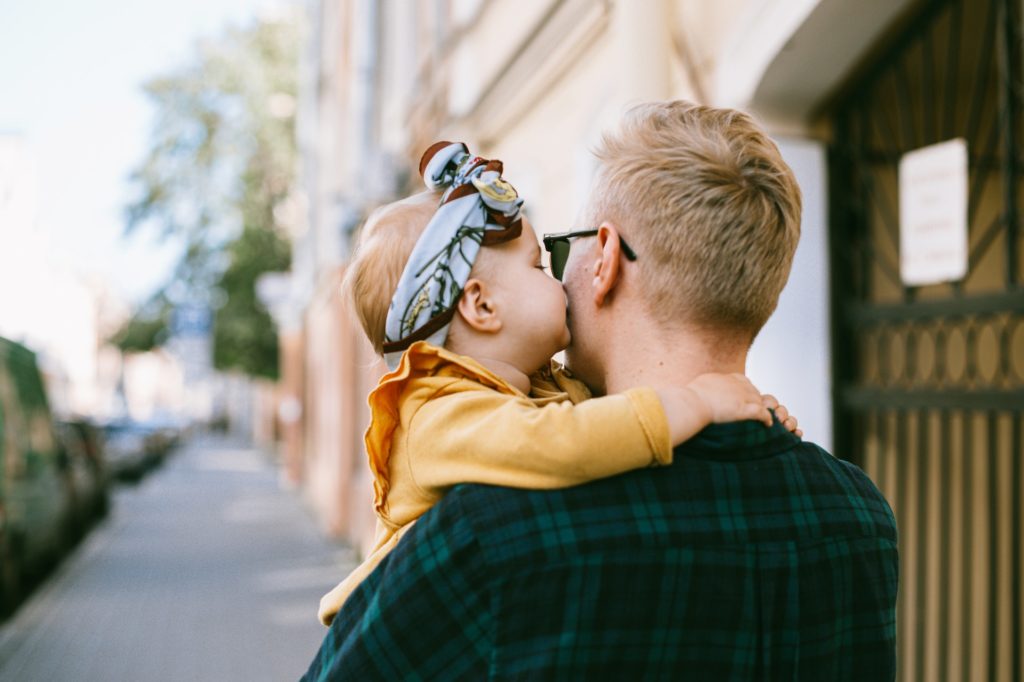 child kissing father's cheek while in his arms