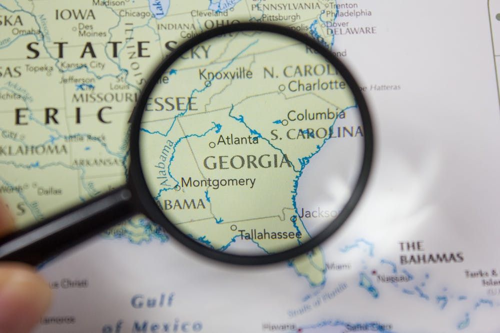 A magnifying glass enhances 'Georgia' on a map, focusing on Atlanta and surrounding states, indicating geography study or travel planning.