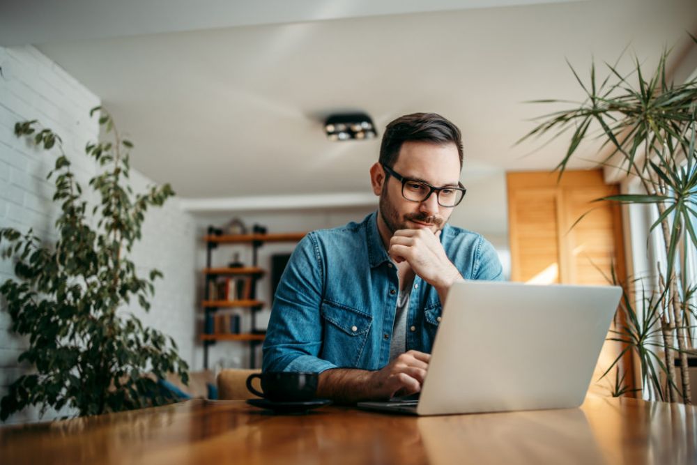 many smiling looking at his laptop which rests on a dark oak kitchen table