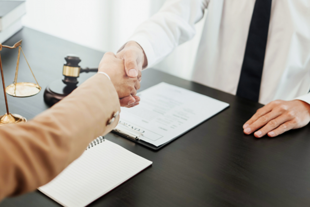 A client shaking hands with an attorney at a across a wooden desk