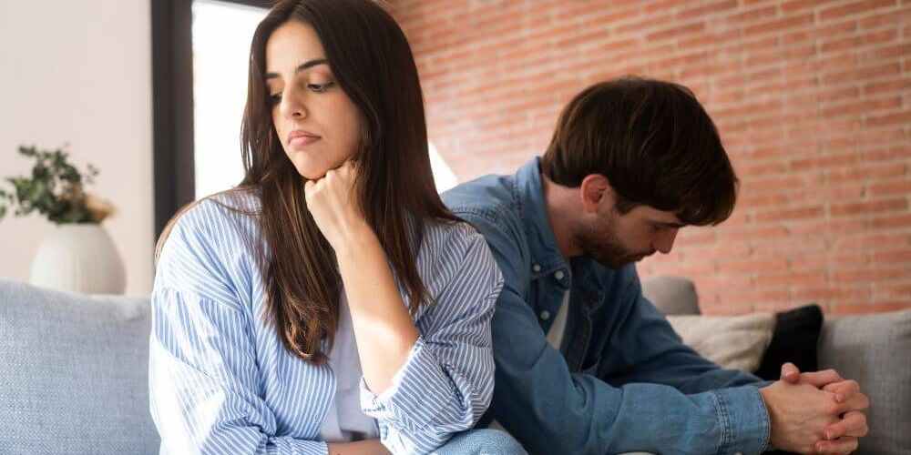 "A couple sitting apart on a couch, both looking distressed and deep in thought, illustrating the emotional strain and contemplation often involved in the decision to pursue a legal separation.