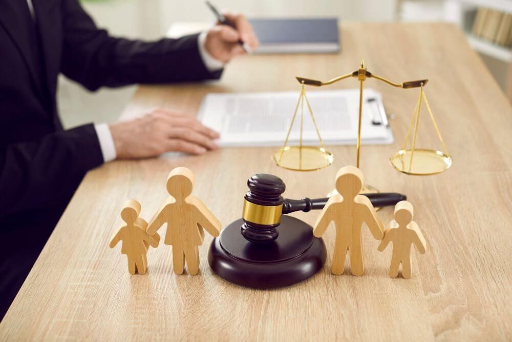 Wooden figures representing a family are positioned near a judge's gavel and a balance scale, symbolizing family law on a courtroom desk.