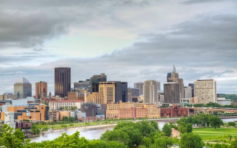 A skyline with diverse buildings under cloud-covered skies, overlooking a river and greenery.