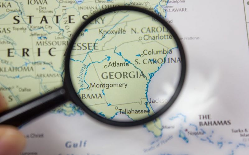 A magnifying glass enhances 'Georgia' on a map, focusing on Atlanta and surrounding states, indicating geography study or travel planning.