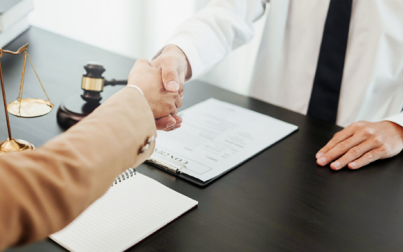 A client shaking hands with an attorney at a across a wooden desk