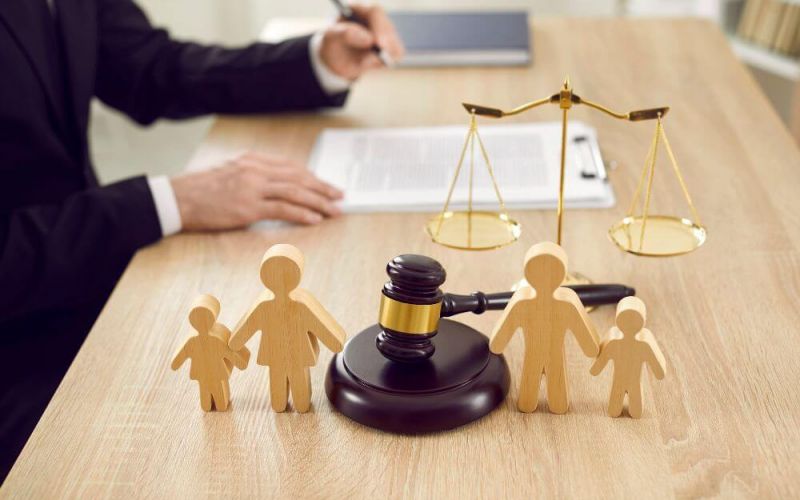 Wooden figures representing a family are positioned near a judge's gavel and a balance scale, symbolizing family law on a courtroom desk.