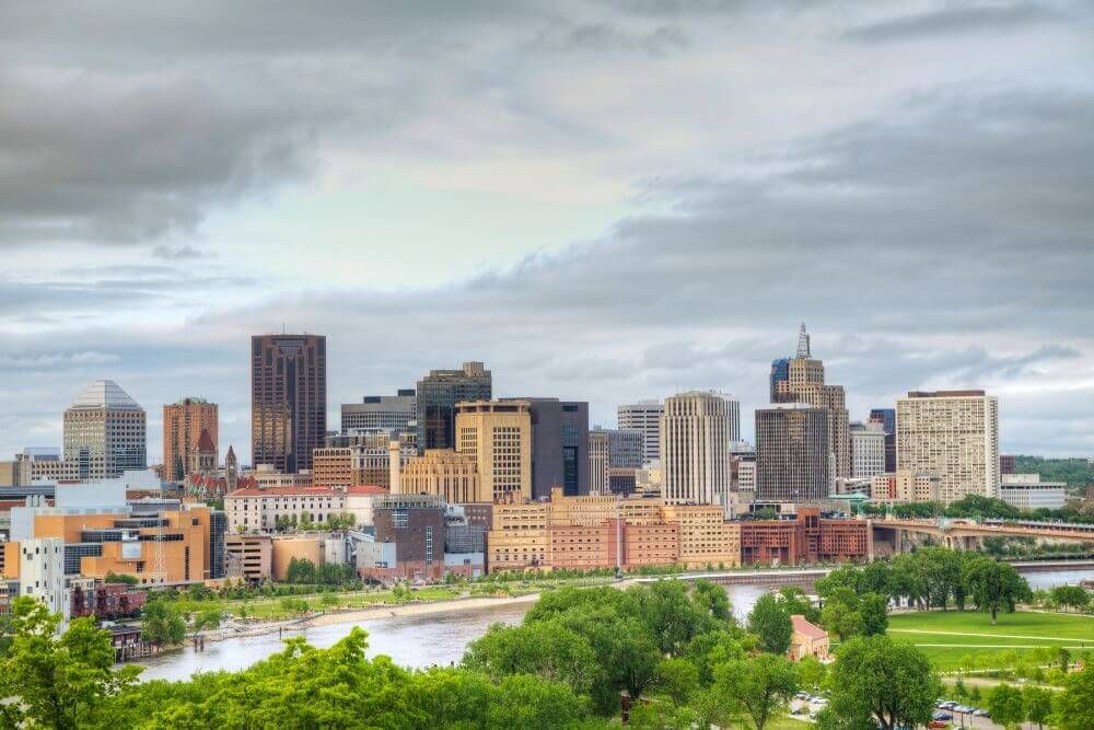 A skyline with diverse buildings under cloud-covered skies, overlooking a river and greenery.