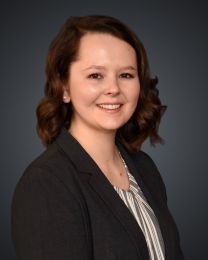 Professional headshot of a smiling woman in a dark blazer against a gray gradient backdrop.