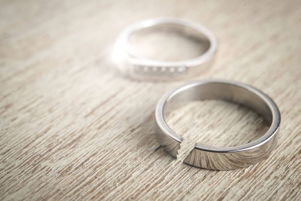 Two rings rest side by side on a textured wooden surface; one is intact and the other is broken in half.