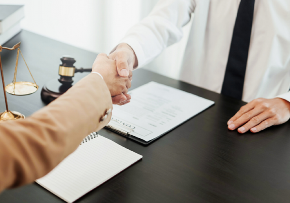 A client shaking hands with an attorney at a across a wooden desk