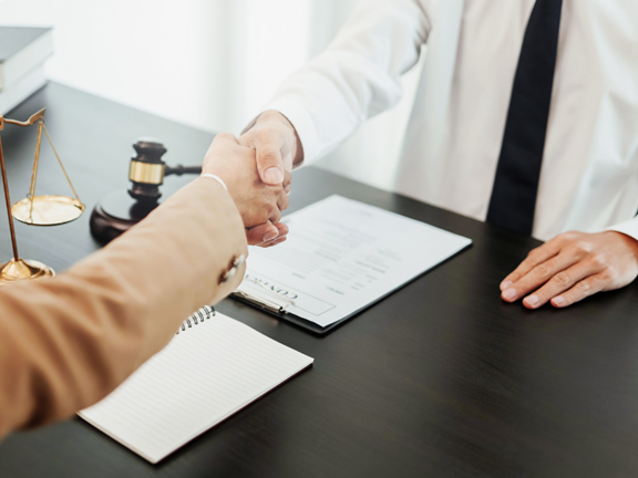 A client shaking hands with an attorney at a across a wooden desk