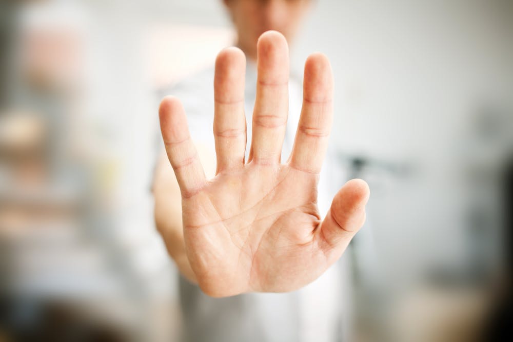 An outstretched hand is gesturing "stop" towards the camera against a blurred background.