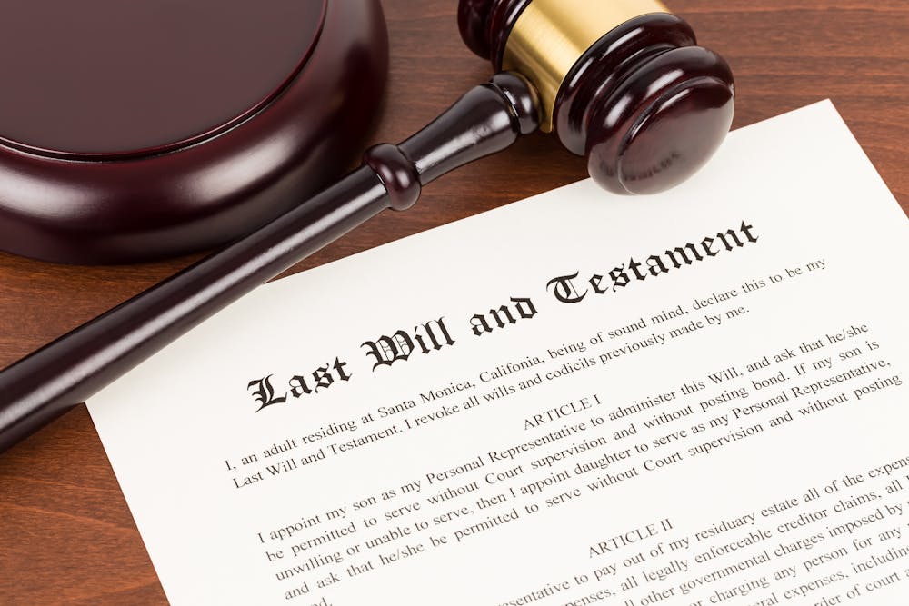 A wooden gavel and sound block rest beside a document titled "Last Will and Testament," symbolizing legal authority and estate planning against a wooden surface. Transcription of visible text: "Last Will and Testament I, an adult residing at Santa Monica, California, being of sound mind, declare this to be my Last Will and Testament. I revoke all wills and codicils previously made by me. ARTICLE I I appoint my son as my Personal Representative to administer this Will; and ask that he/she be permitted to serve without Court supervision and without posting bond. If my son is unwilling or unable to serve, then I appoint my daughter as my Personal Representative, and ask that he/she be permitted to serve without Court supervision and without posting [...]"