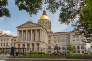 Georgia capital building with a golden dome stands prominently under a blue sky, framed by lush foliage in a city environment.