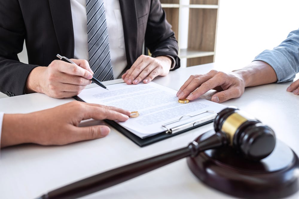 Close-up view of a lawyer guiding a couple through the legal separation process, highlighting the signing of documents and the division of assets with wedding rings and a gavel on the table, symbolizing the formal and legal nature of their separation.