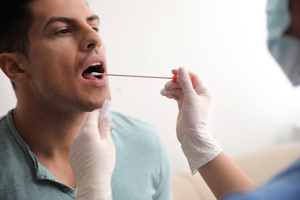 A man is getting a throat swab by a person in protective gloves, suggesting a medical test or examination in a clinical setting.