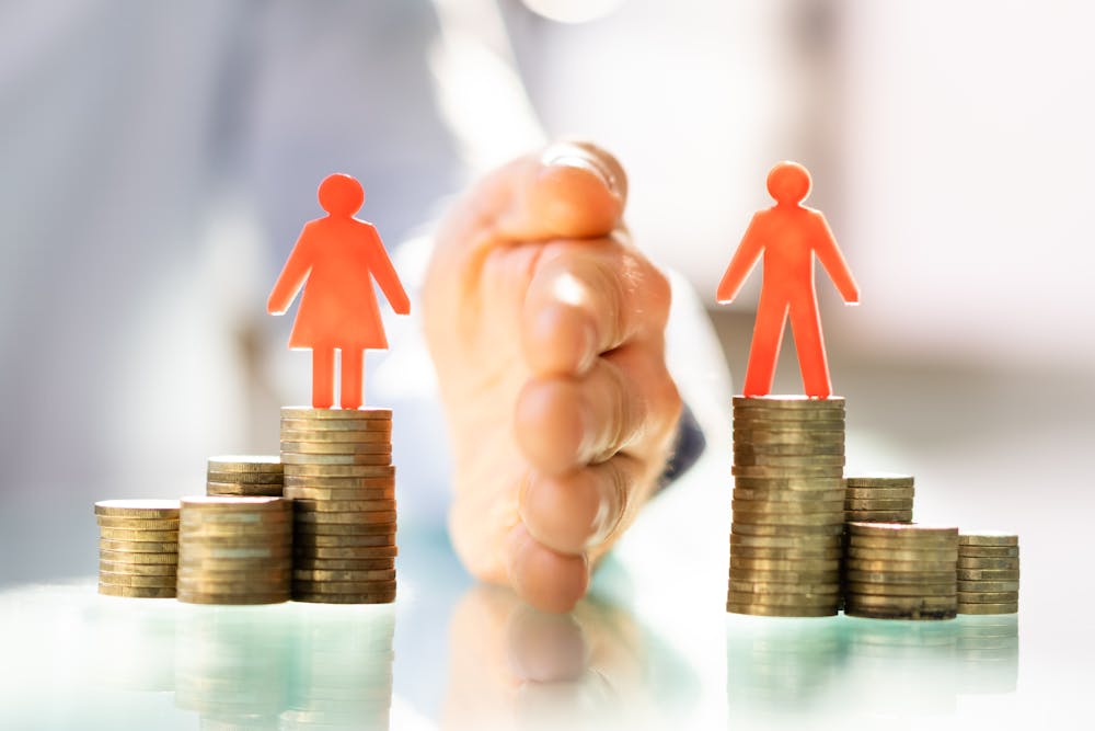 Red silhouettes of a man and a woman stand atop uneven stacks of coins with a hand reaching towards them, possibly implying financial growth or inequality.