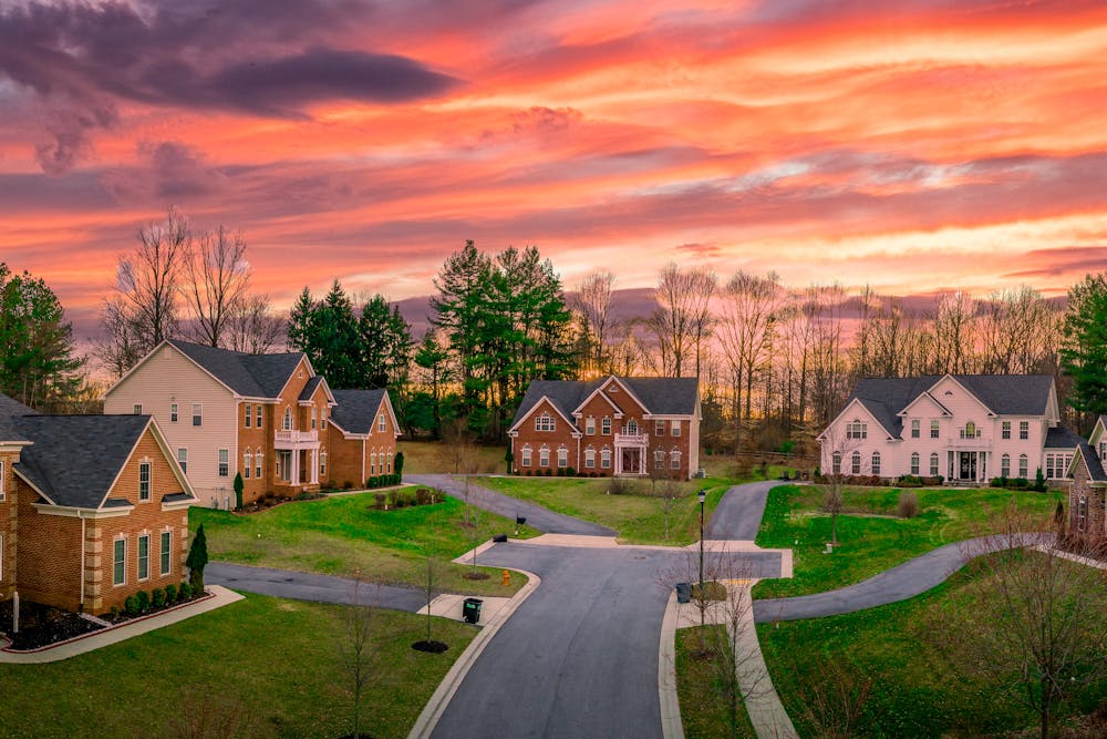 Suburban houses at dusk with a vivid orange and pink sky, lined by bare trees, on a tranquil, curved street.