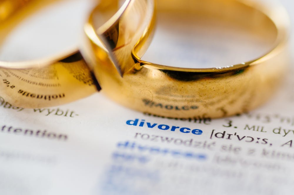 Two golden rings overlap on a document with the word "divorce" prominently visible, suggesting the dissolution of a marriage.