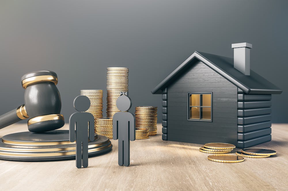 A judge's gavel, two silhouetted figures, a stack of coins, and a house model sit on a wooden surface against a grey backdrop, suggesting legal or financial themes.