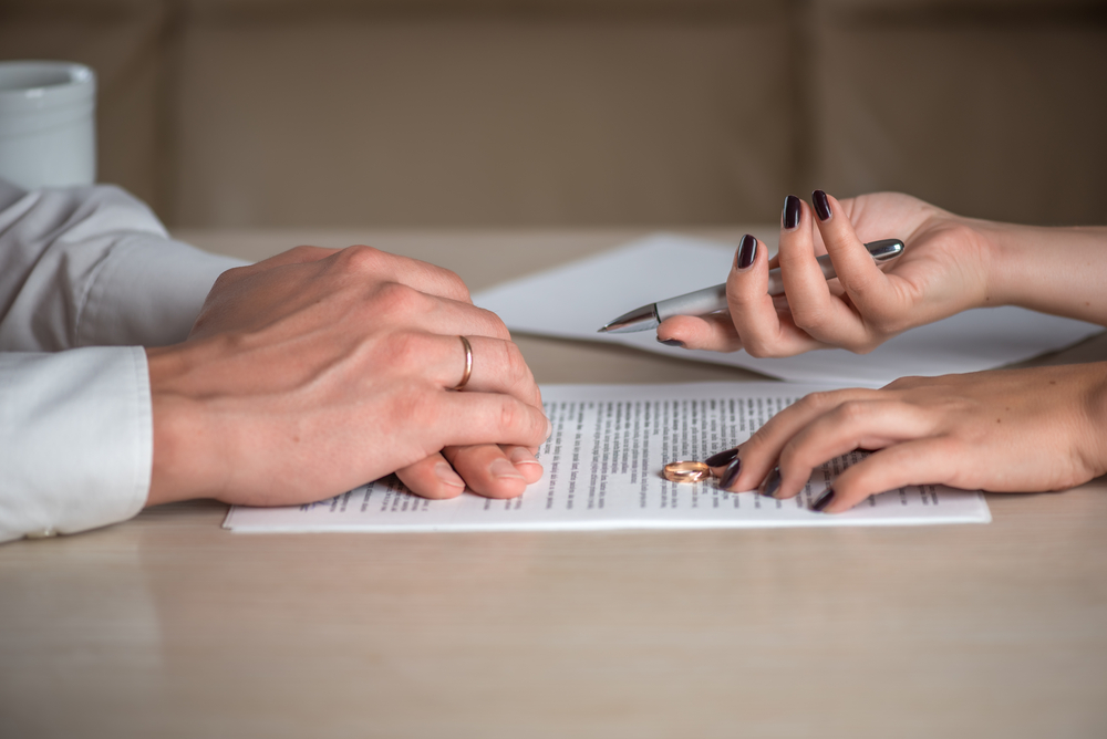 Up-close of a husband's and wife's hands signing divorce papers