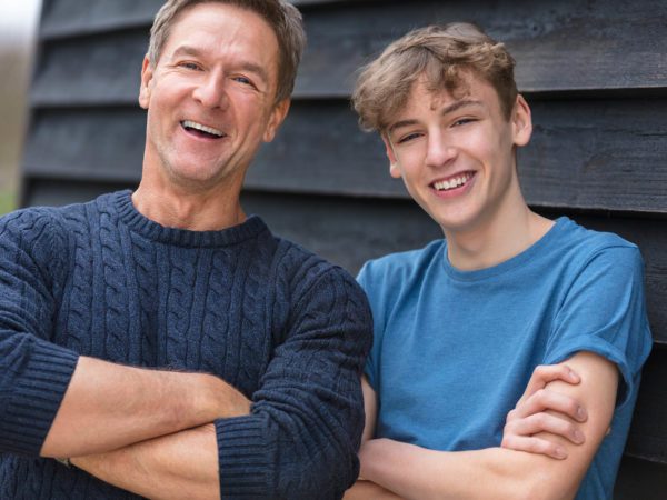 Portrait shot of a happy middle aged man father male arms folded with his teenage boy son