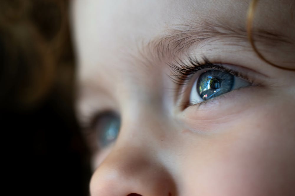 Close-up of a child's eye reflecting light, with delicate skin texture and fine eyelashes. The child appears focused, in a dimly lit setting.