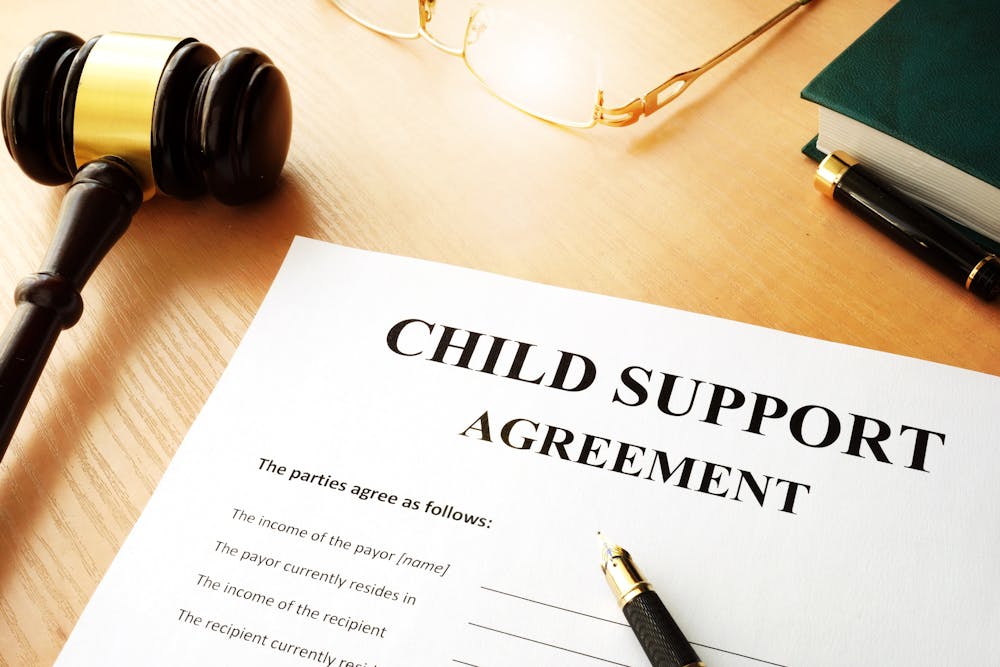 A "CHILD SUPPORT AGREEMENT" document is displayed, next to a judge's gavel, glasses, and legal books on a wooden surface.