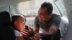 father putting son in car seat
