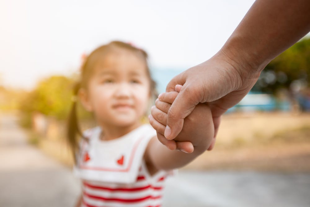 A young child holding an adult's hand, evoking trust and guidance, with a blurred outdoor backdrop.