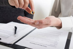 A hand is passing a golden wedding ring to another hand above a signed divorce decree, indicating the dissolution of marriage. A pen rests beside the legal document.