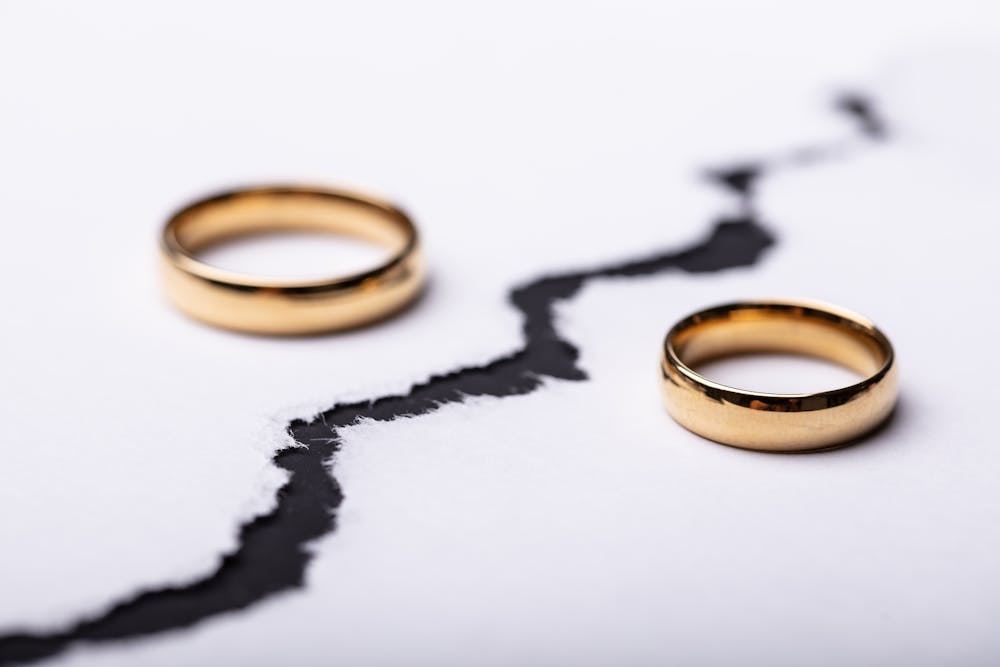 Two golden rings sit on a cracked white surface that separates them, symbolizing a break or division. The background is plain and white.