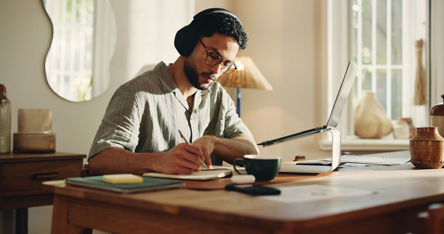 Man at home writing notes from laptop